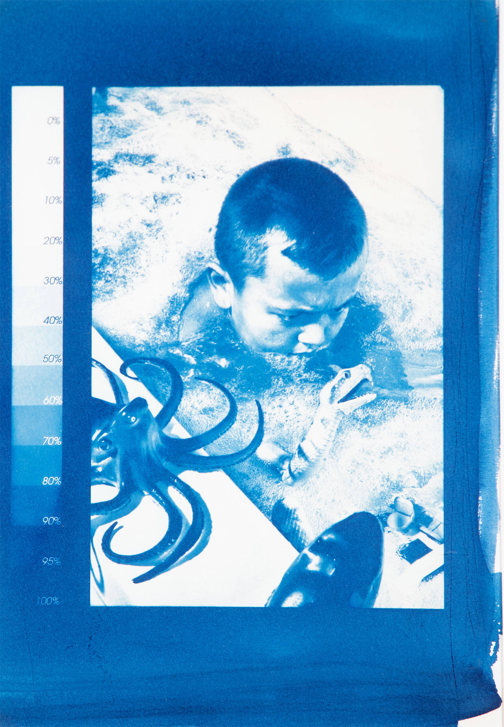 Blue cyanotype image of a young boy in the bathtub with a octopus and boat toy.